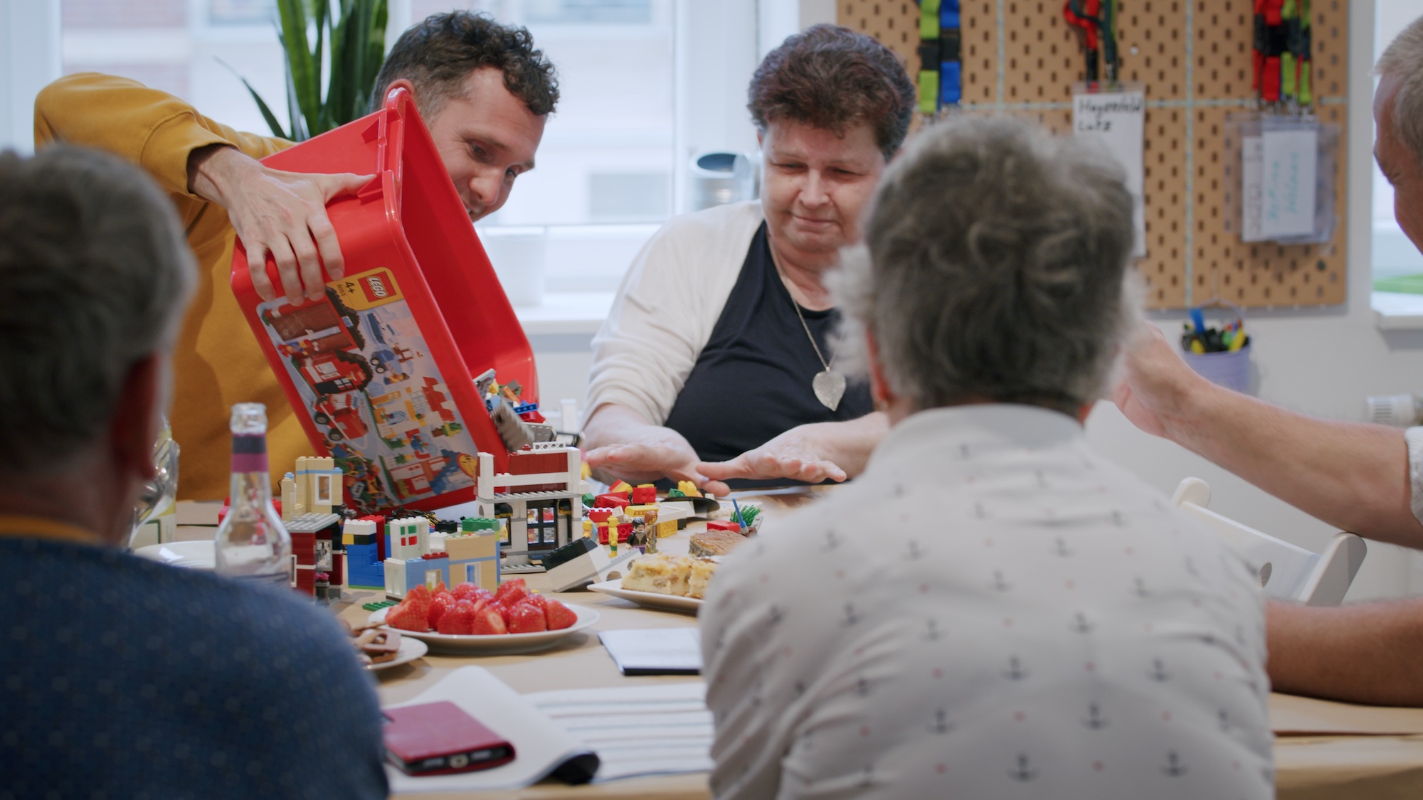 Das Bild zeigt Jun-Prof. Dr. Andreas Bischof in einer Gruppe mit älteren Menschen. Auf dem Tisch liegt Lego. Er schüttet eine Kiste mit weiteren Bausteinen aus.